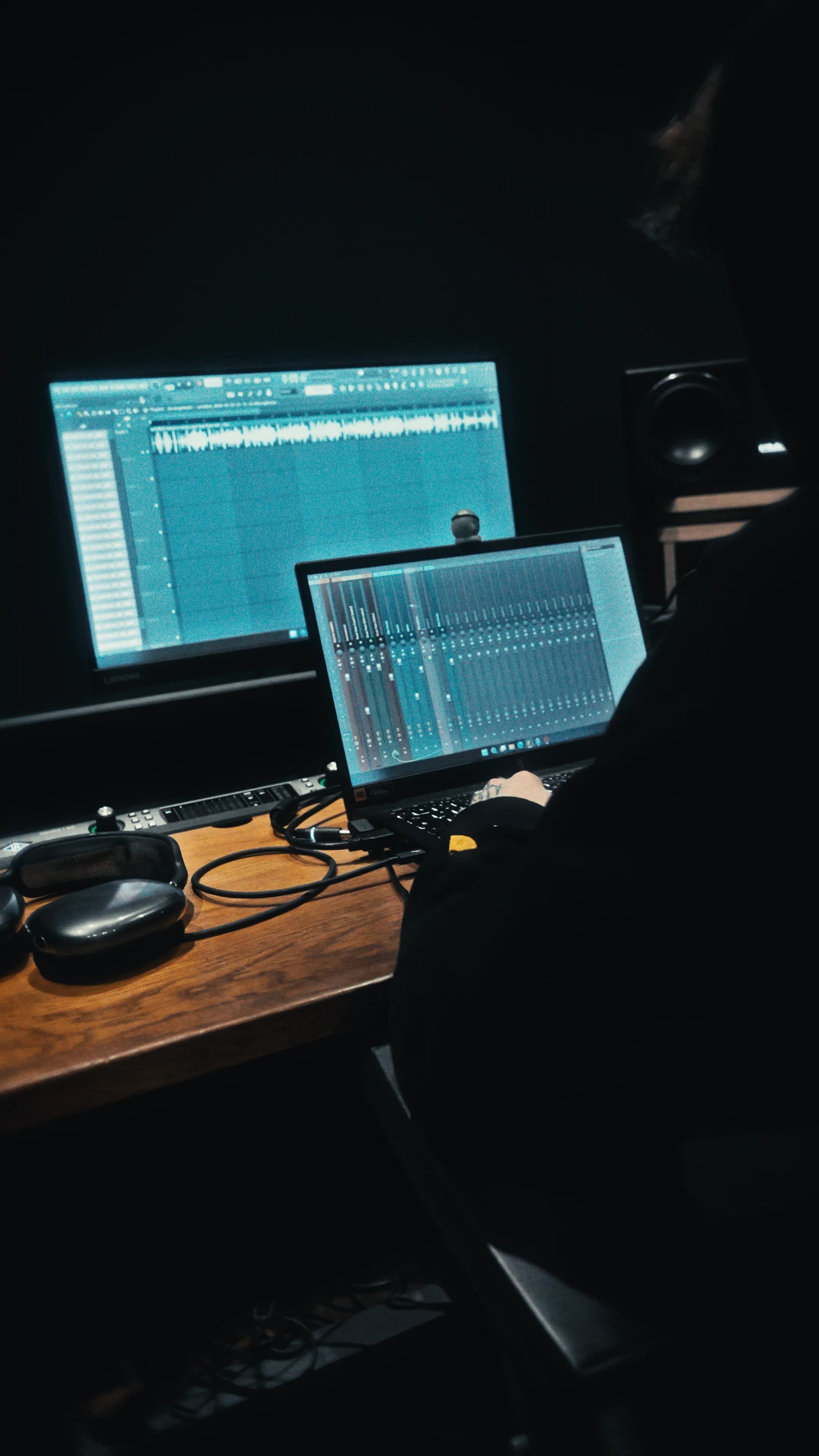 Ingénieur au poste de travail de Coin Bleu Studio : écran du séquenceur, ordinateur portable et casque sur le bureau en bois